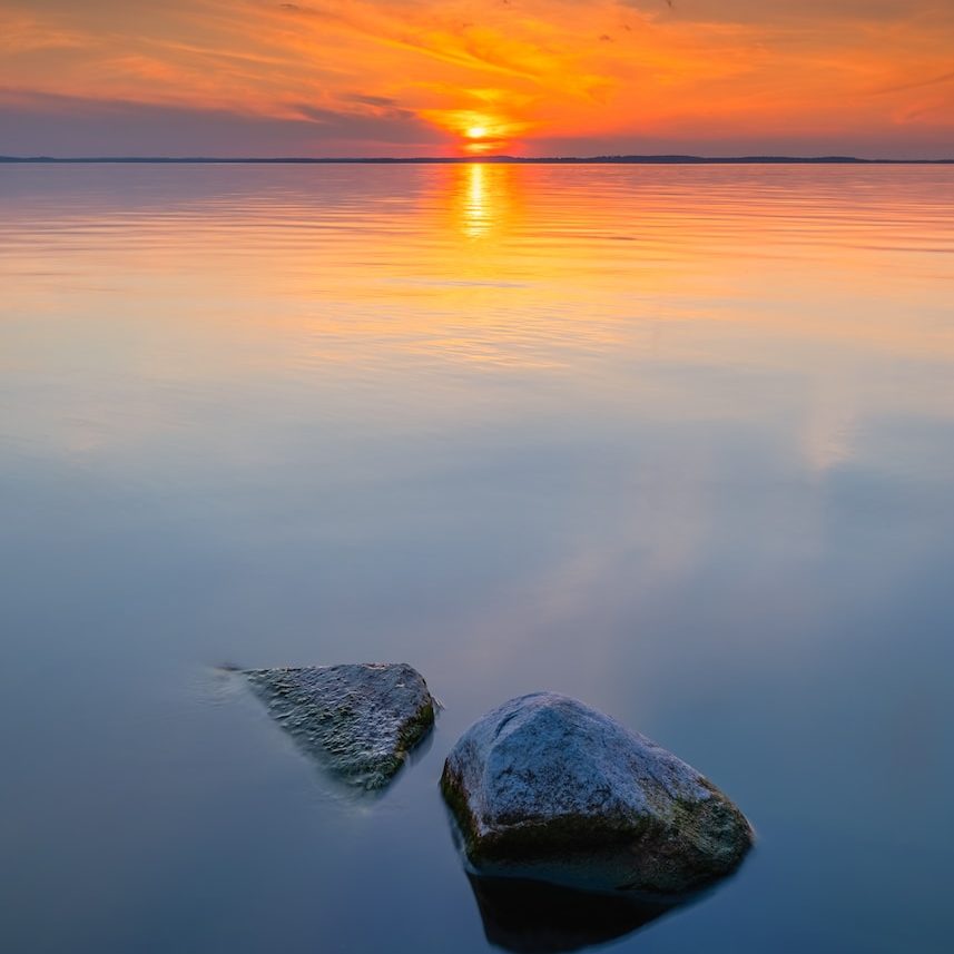 gray rock on body of water during sunset